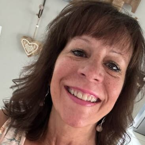 Woman with brown hair and bangs smiles, wearing pink earrings.