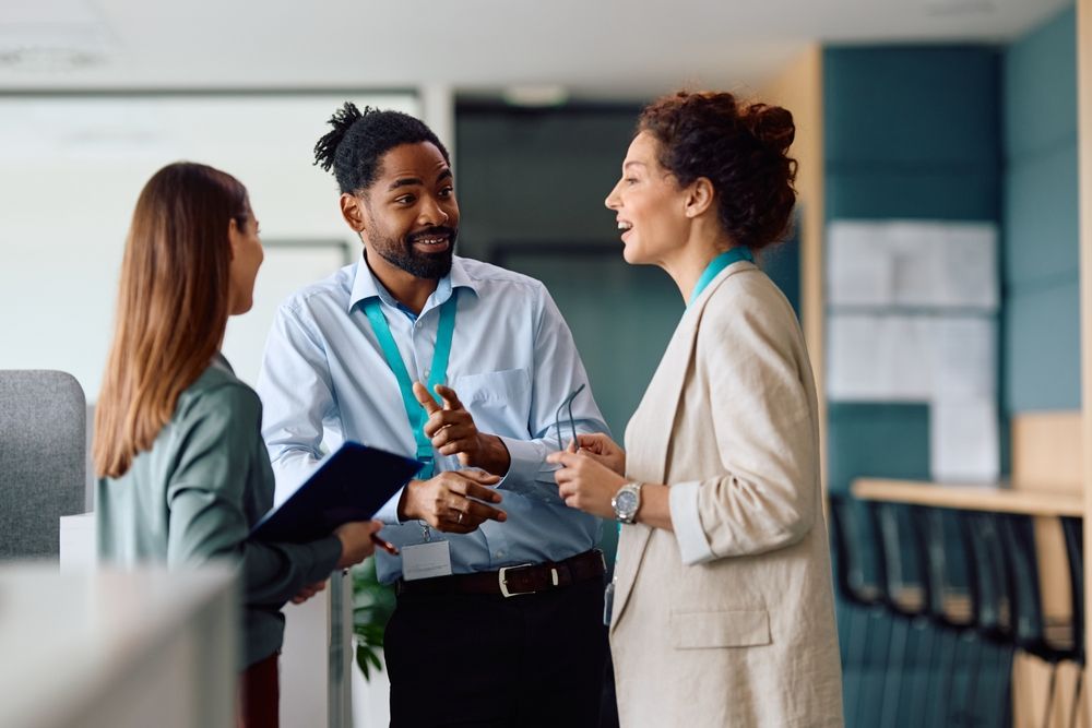 A group of people are standing in an office talking to each other.