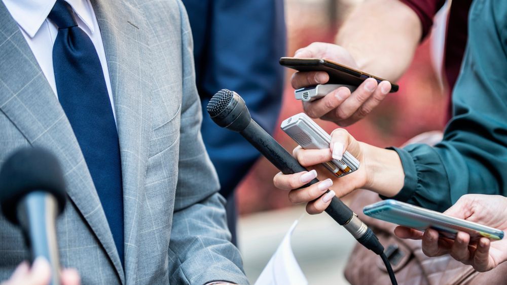 A man in a suit and tie is being interviewed by a group of people holding microphones.