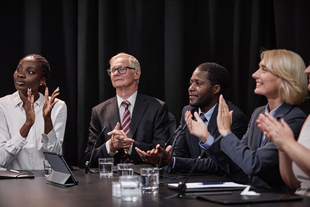 A group of people are sitting around a table applauding.