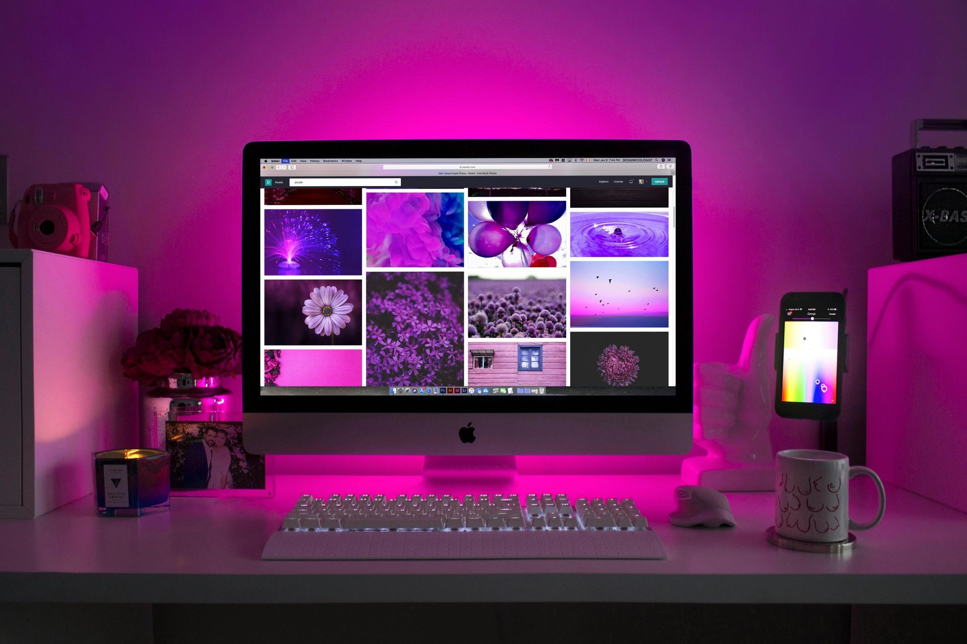 Desktop computer on a white desk, with a pink ambient light. Screen shows images of purple items.