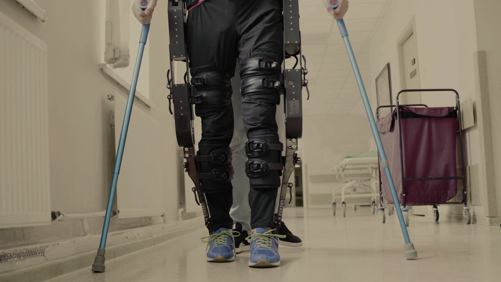 A person wearing a prosthetic leg and crutches is walking down a hallway.