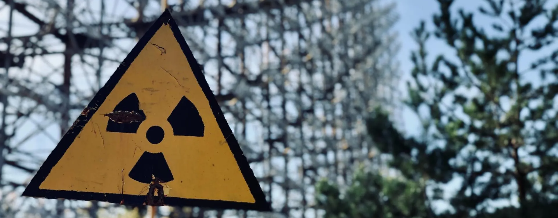 A yellow and black radioactive sign is hanging from a fence.