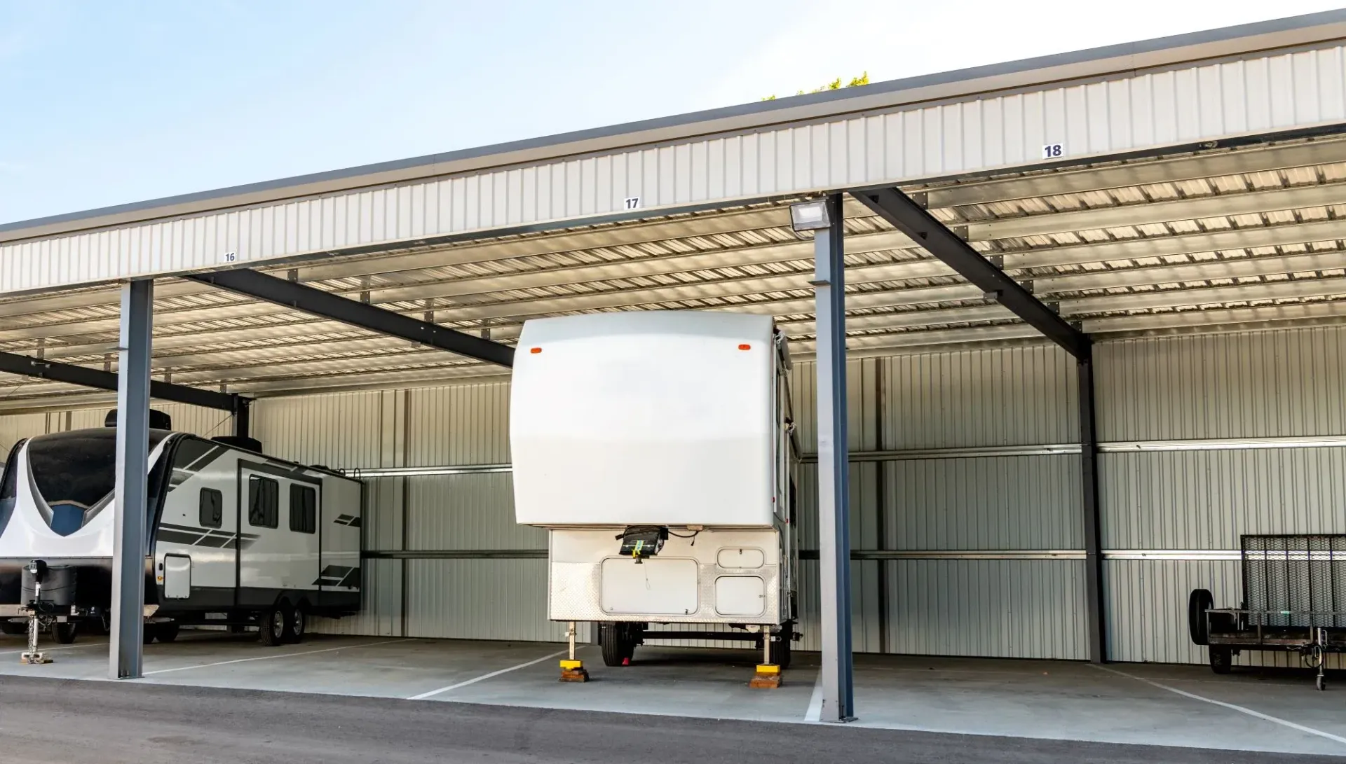 RVs parked under a metal awning at a storage facility.