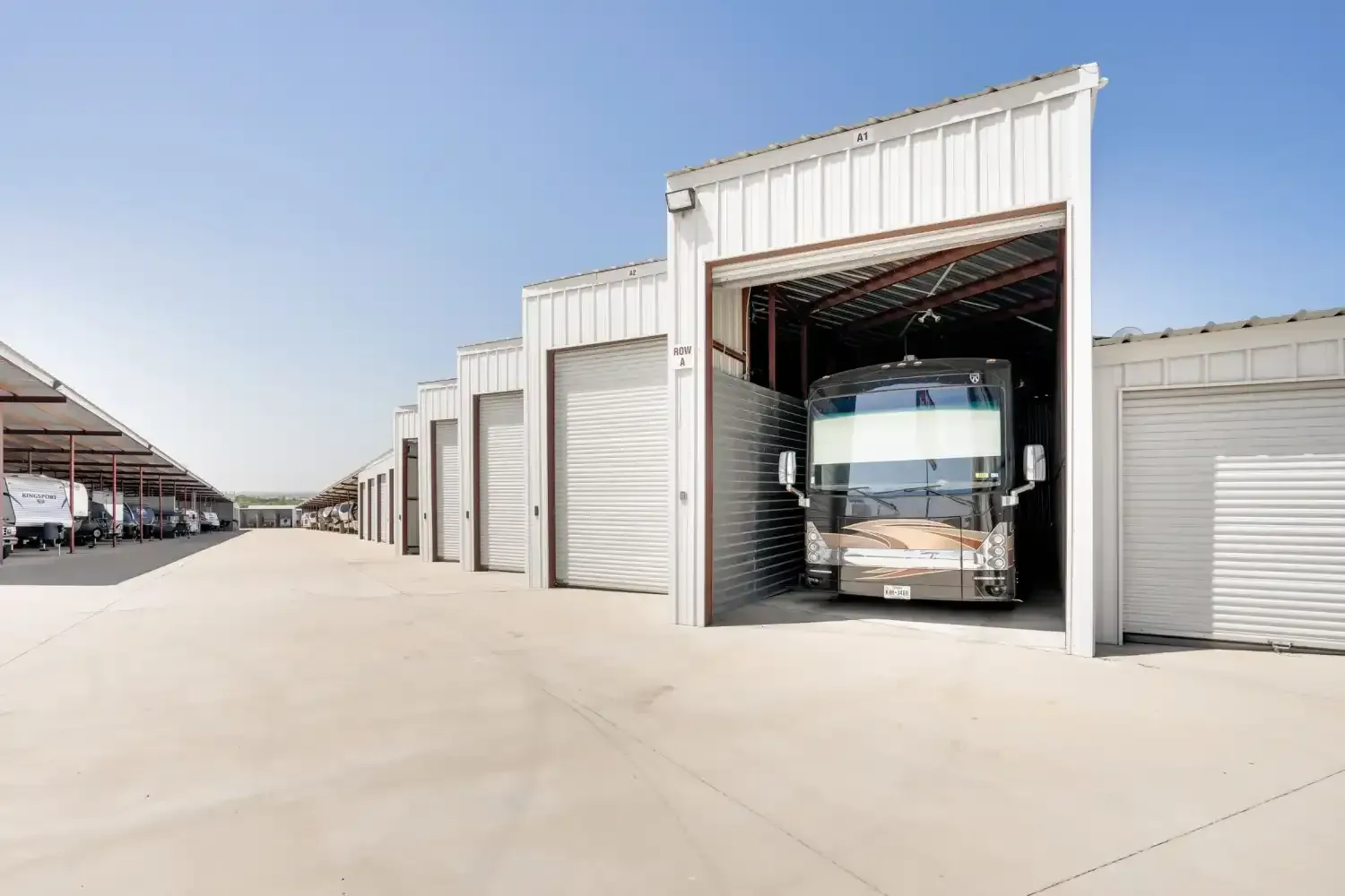 Motorhome in a covered storage unit, lined with others, on a sunny day.