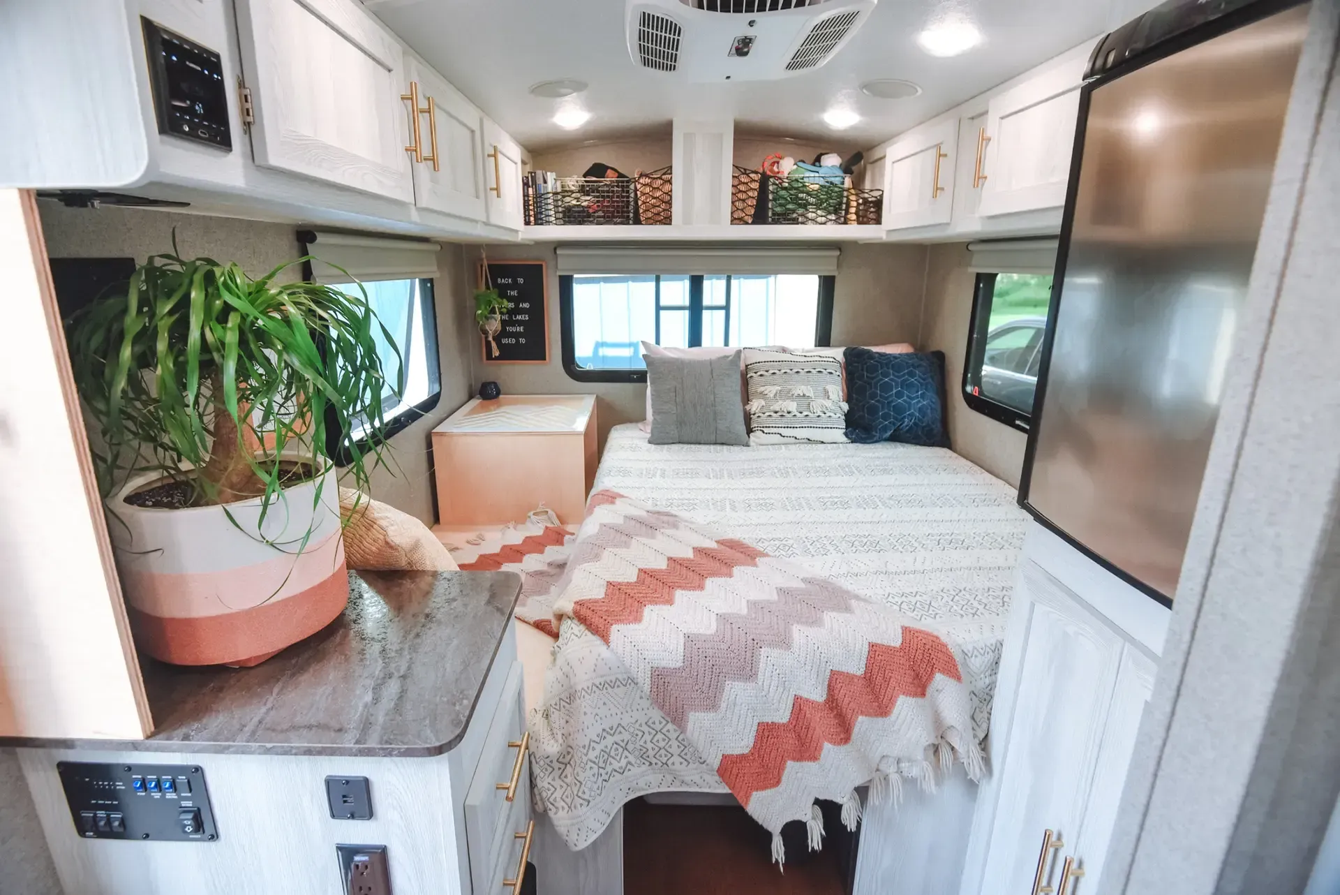 Cozy camper interior with a bed, cabinets, and a potted plant. Soft colors and warm lighting.