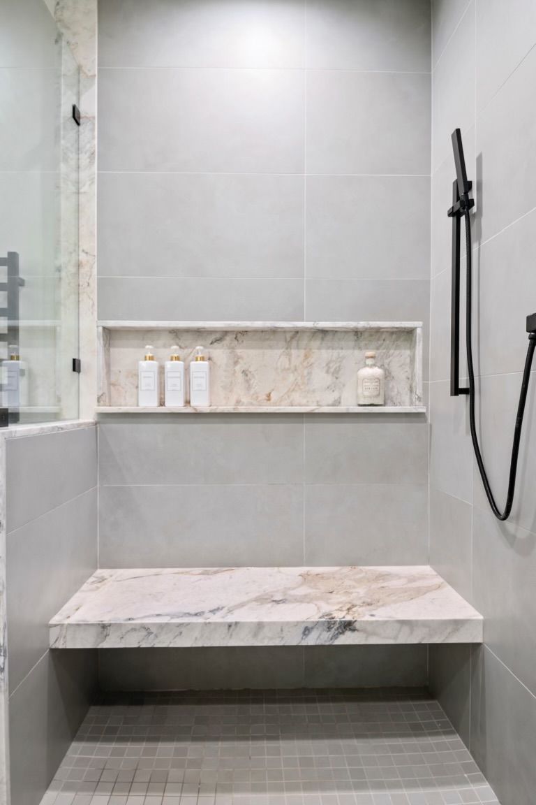 There is a bench in the shower with a shower head.
