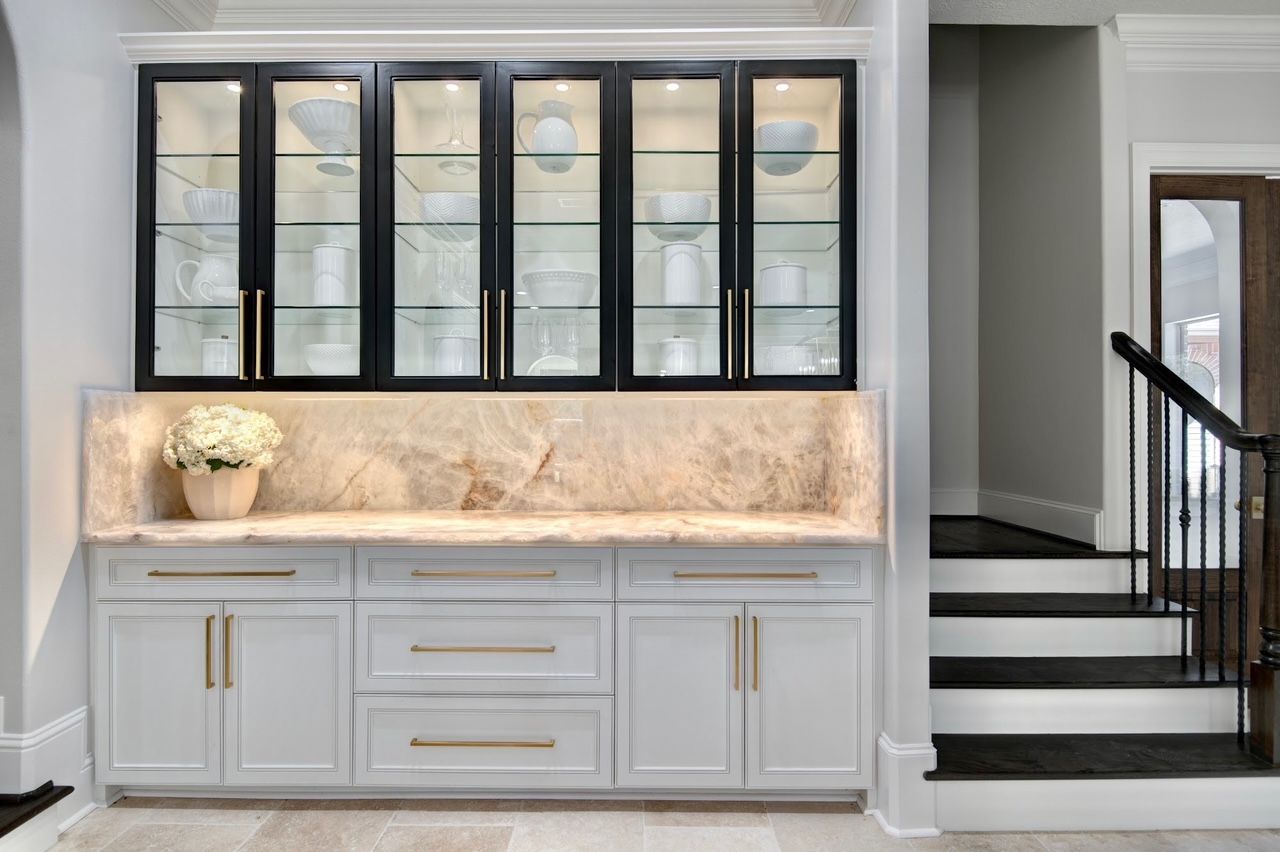 A kitchen with white cabinets and black glass doors next to a staircase.