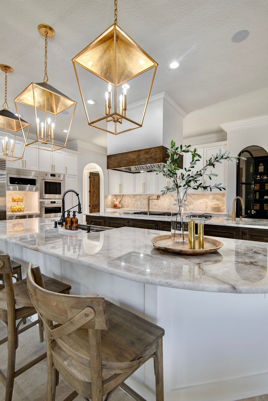 A kitchen with white cabinets , marble counter tops , stools , and a large island.