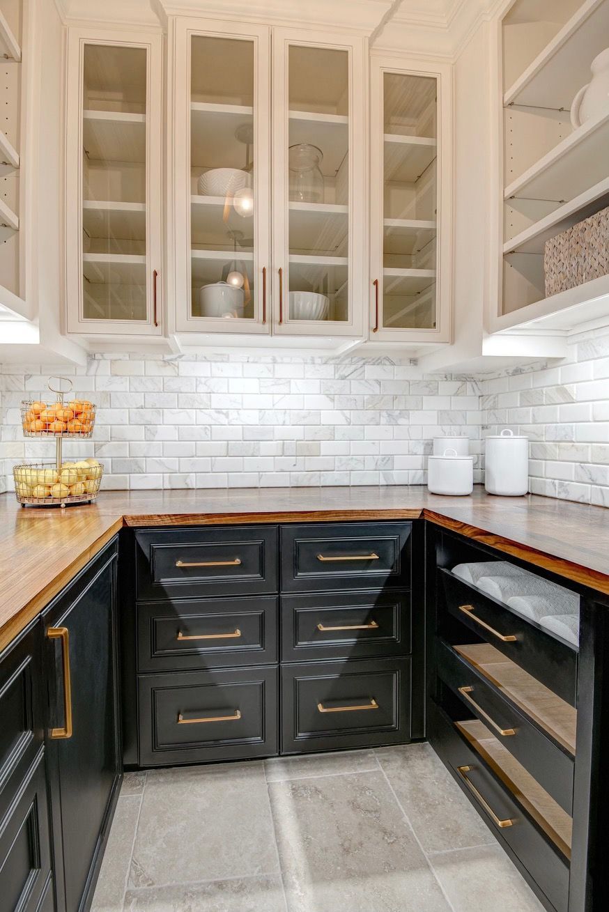 A kitchen with black cabinets and white cabinets with glass doors.