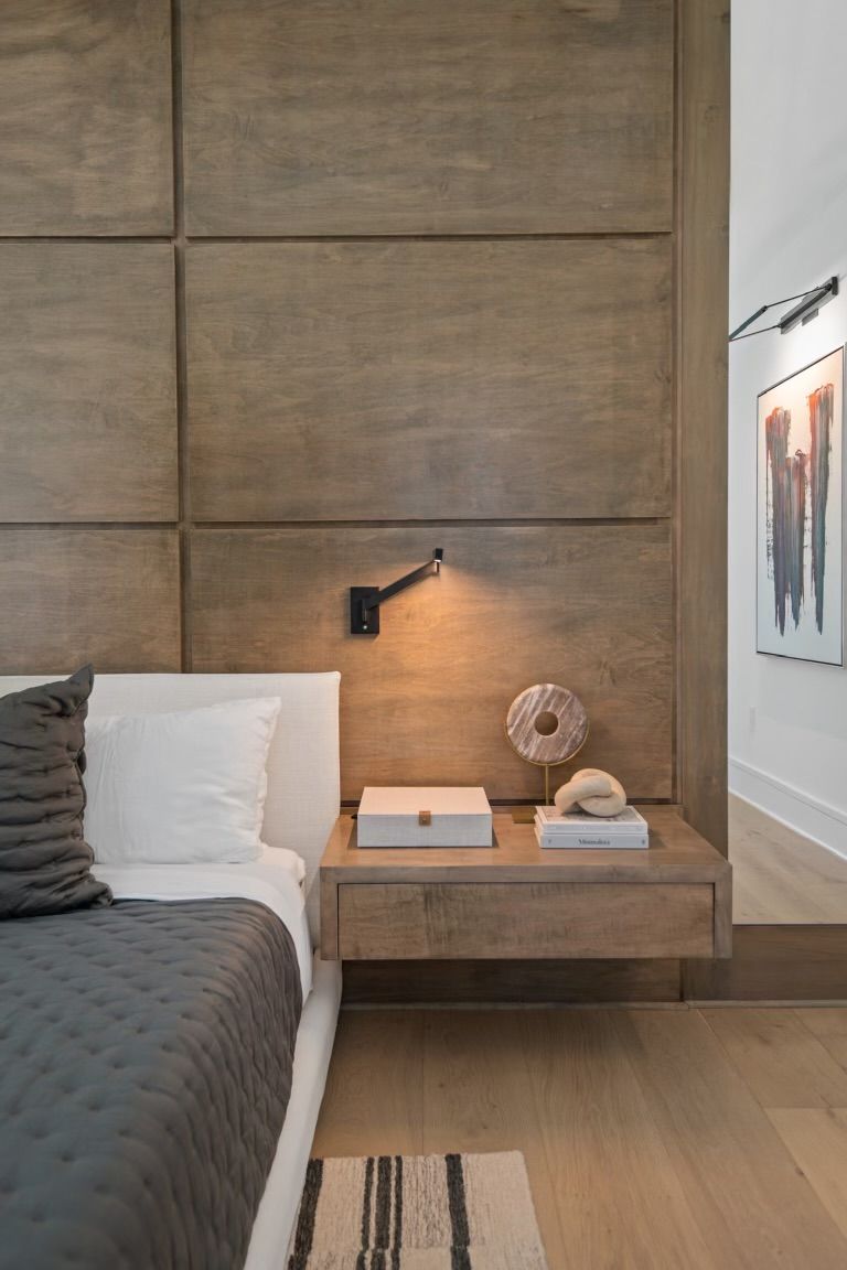 A bedroom with a bed , nightstand , and wooden wall.