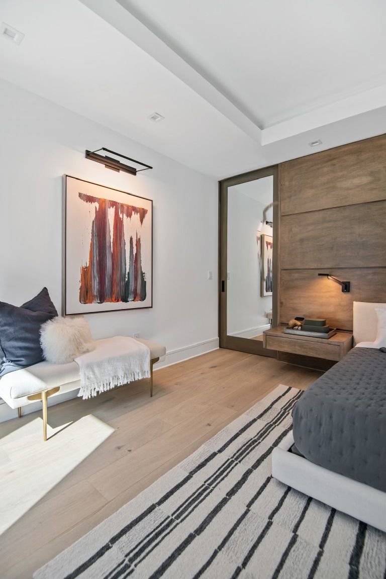 A bedroom with a bed , bench , rug and painting on the wall.