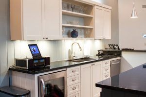 A kitchen with white cabinets and black counter tops and a stainless steel refrigerator.