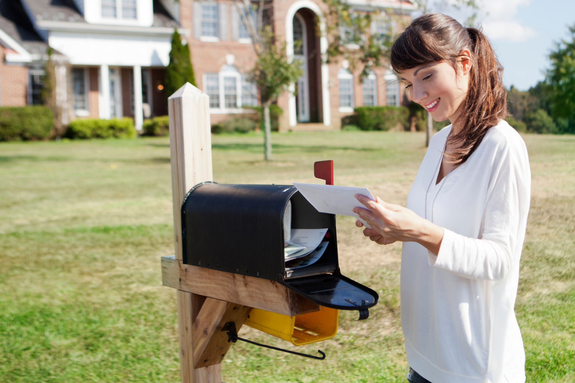 A woman is putting a letter in a mailbox in front of a house.