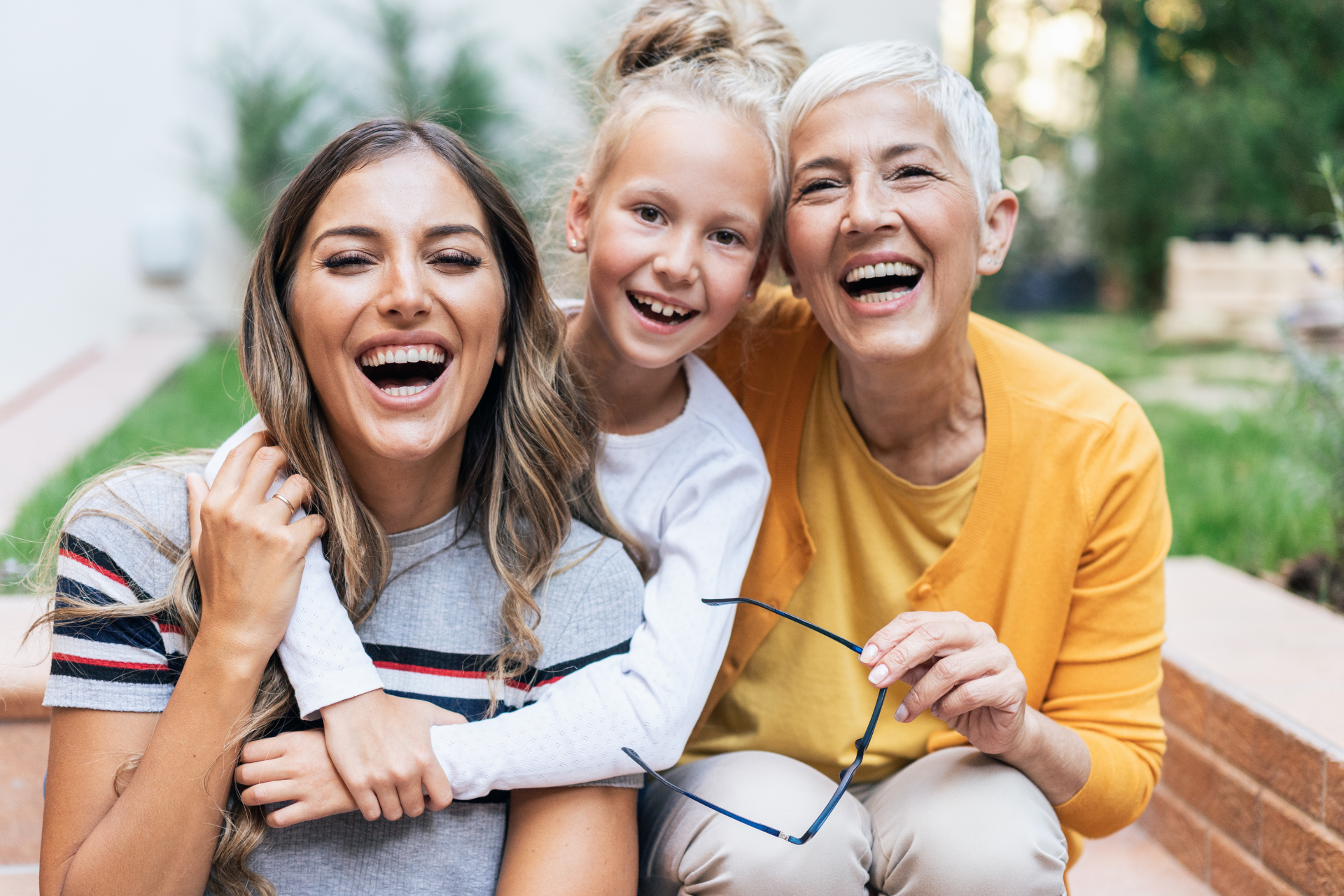 Three generations 2 women and a little girl are sitting on a bench and laughing.