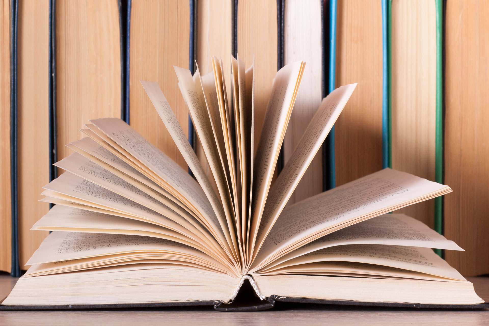 Open book with fanned-out pages in front of a shelf of closed books.