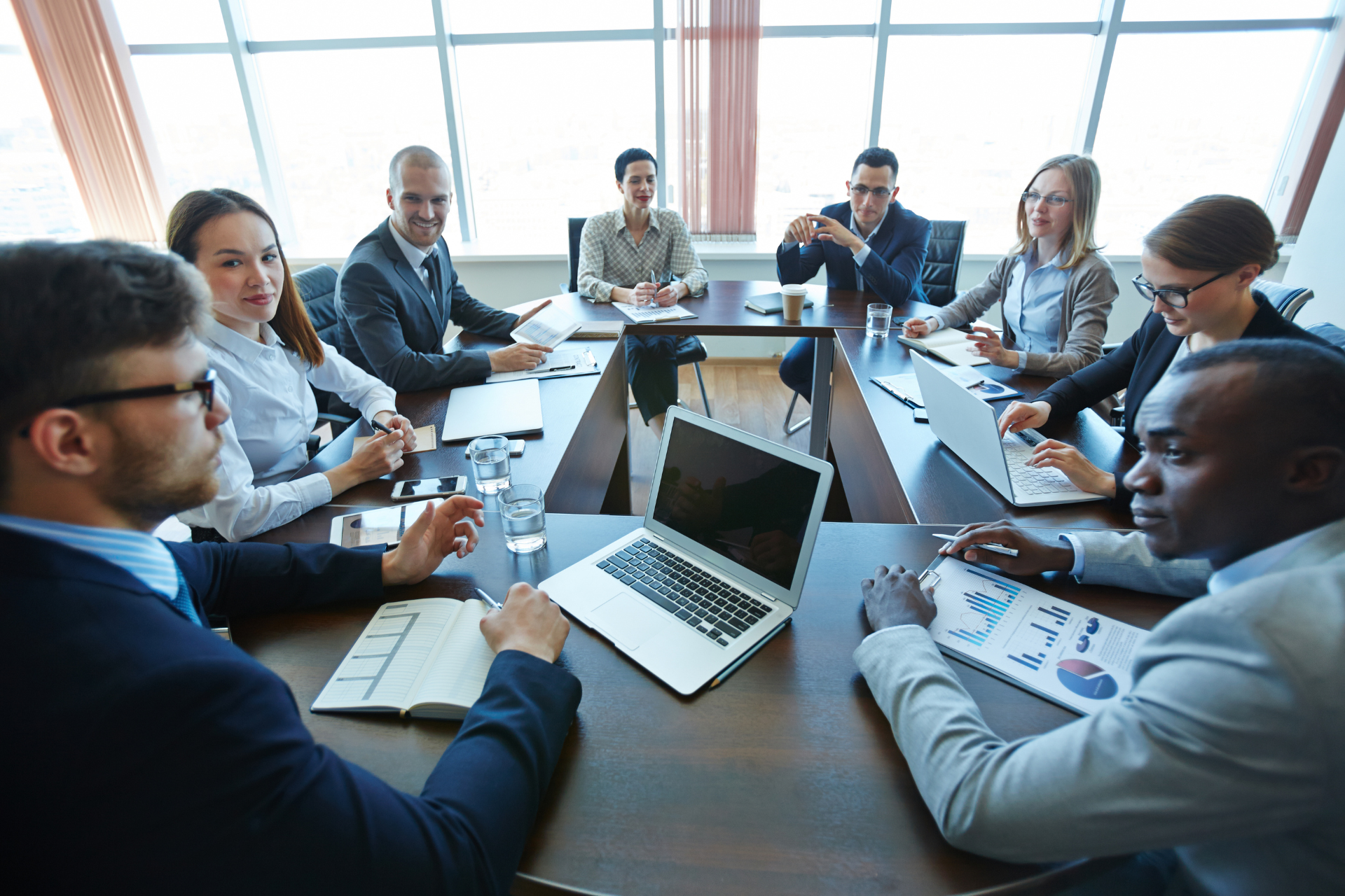 A group of business people are sitting around a conference table with laptops.