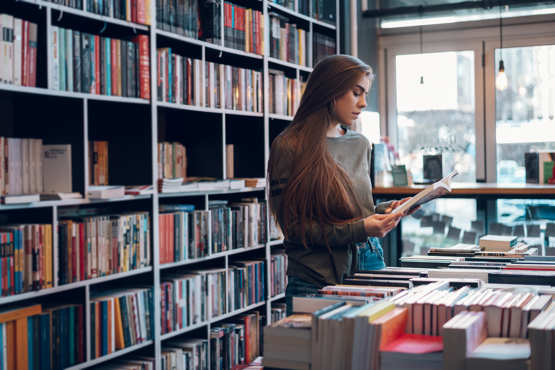 Woman in a library browsing books, standing near shelves.