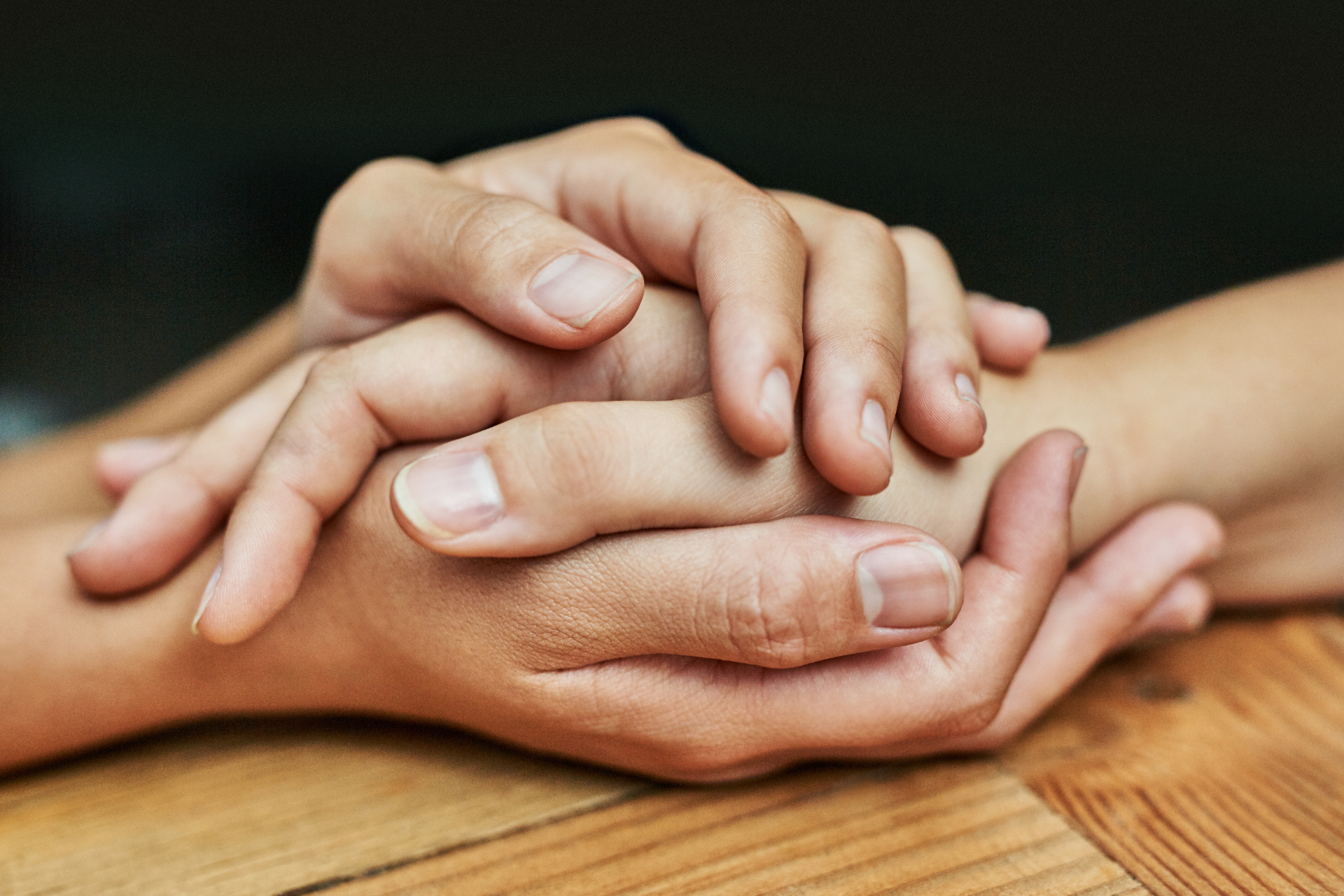 Two people are holding hands on a wooden table.