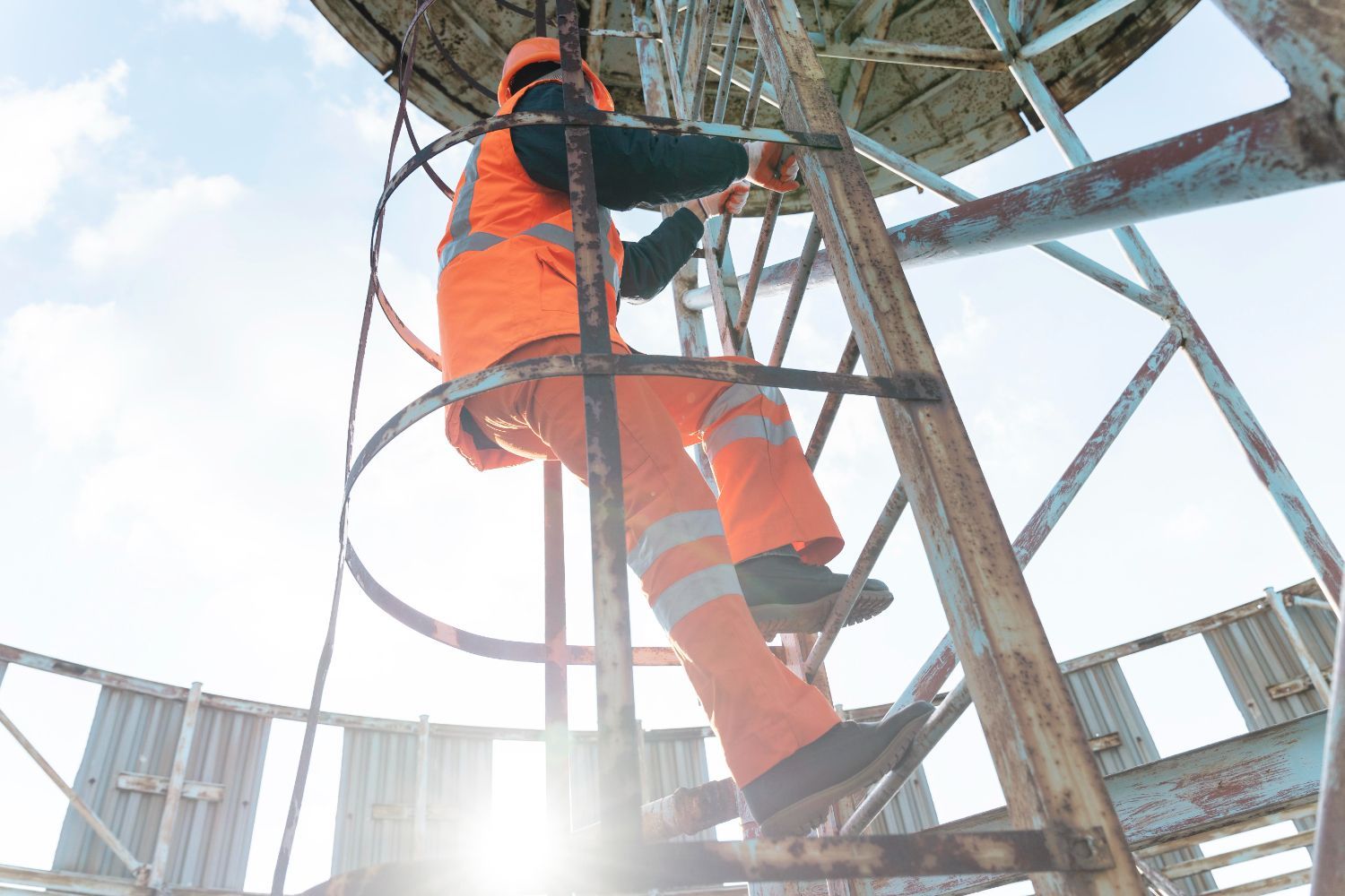 A man is climbing up a metal ladder to a water tower.