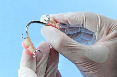 A Person Wearing Gloves is Holding a Denture in Their Hand — Burleigh Heads Denture Clinic Gold Coast in Burleigh Heads, QLD