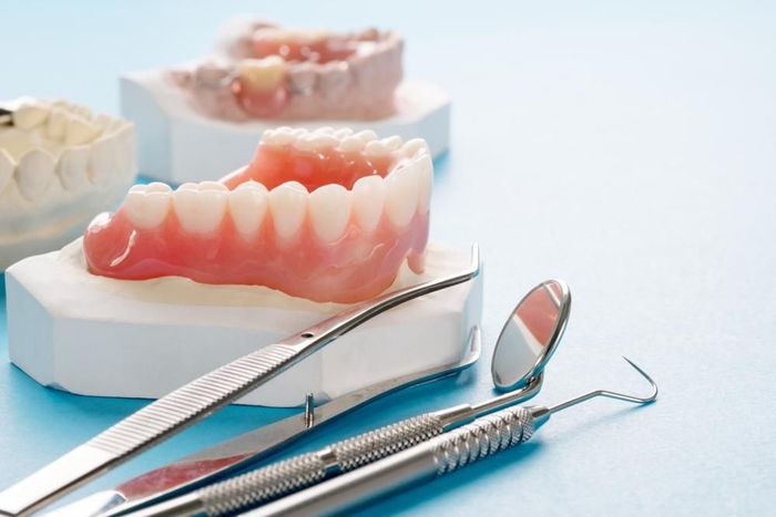 A Pair of Dentures and Dental Instruments on a Blue Surface — Burleigh Heads Denture Clinic Gold Coast in Burleigh Heads, QLD A Pair of Dentures and Dental Instruments on a Blue Surface — Burleigh Heads Denture Clinic Gold Coast in Burleigh Heads, QLD