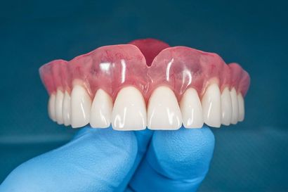A Person is Holding a Full Denture in Their Hand — Burleigh Heads Denture Clinic Gold Coast in Burleigh Heads, QLD