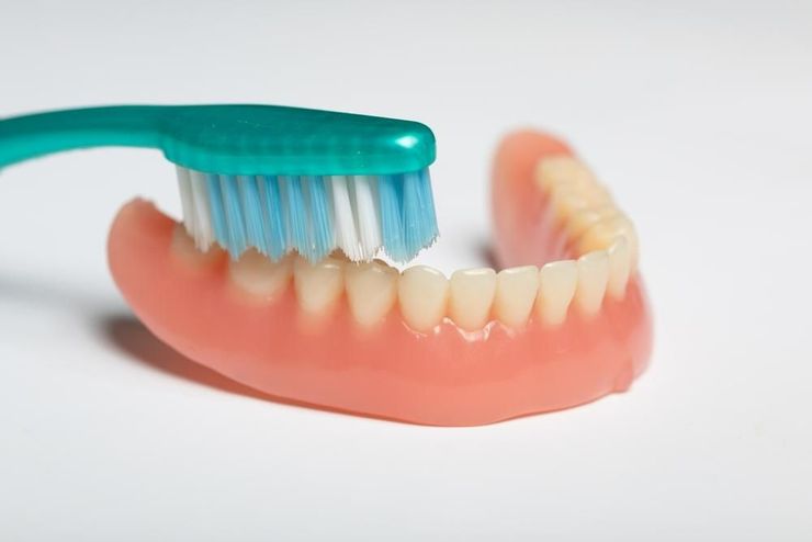 A Person is Brushing a Denture With a Toothbrush — Burleigh Heads Denture Clinic Gold Coast in Burleigh Heads, QLD