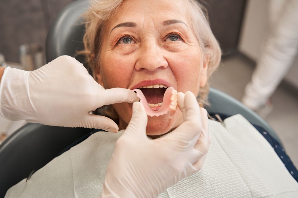 An elderly woman is sitting in a dental chair while a dentist examines her teeth. — Burleigh Heads Denture Clinic Gold Coast in Burleigh Heads, QLD