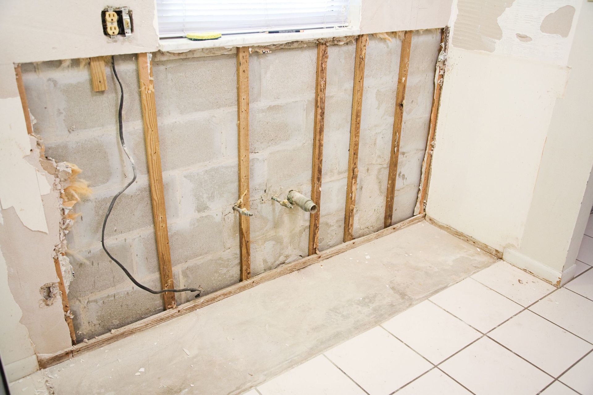A section of a room's wall is stripped to its concrete block frame with visible wooden studs and electrical wiring.