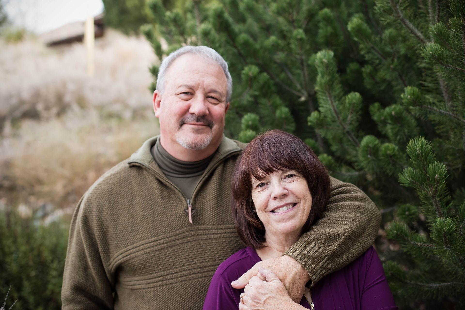 A man and a woman are posing for a picture in front of a christmas tree.