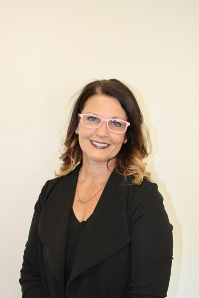 A woman wearing glasses and a black jacket is smiling for the camera.