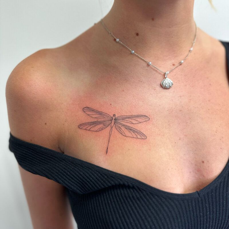 A woman has a dragonfly tattoo on her chest.