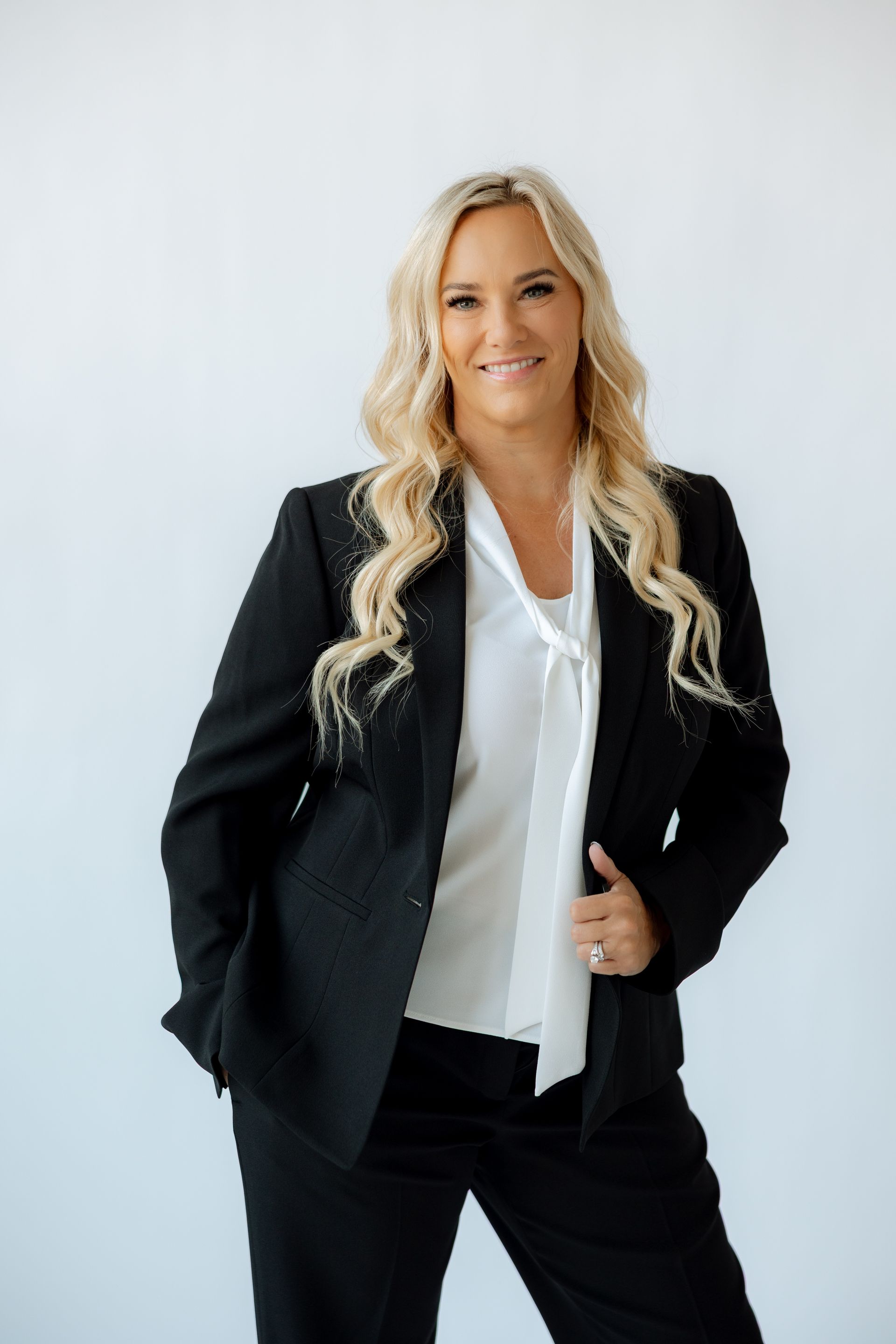 A woman in a white jacket and white pants is sitting in a chair and smiling.