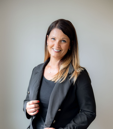 A woman wearing glasses and a black jacket is smiling for the camera.