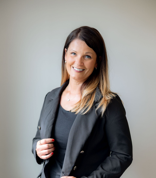 A woman wearing glasses and a black jacket is smiling for the camera.