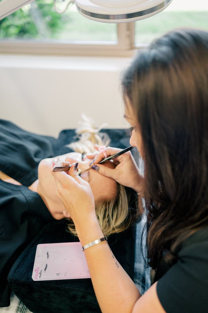 A woman is applying eyelash extensions to a woman 's eye.