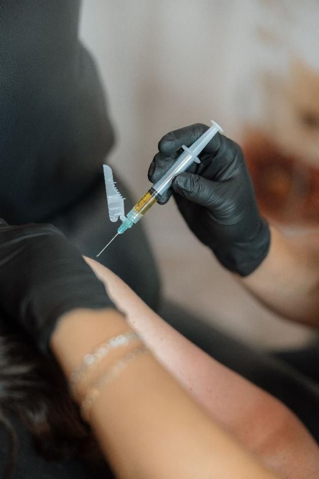 A person wearing black gloves is holding a syringe and a bottle.