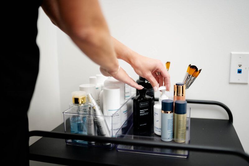 A woman is reaching for a bottle of lotion on a cart filled with cosmetics.