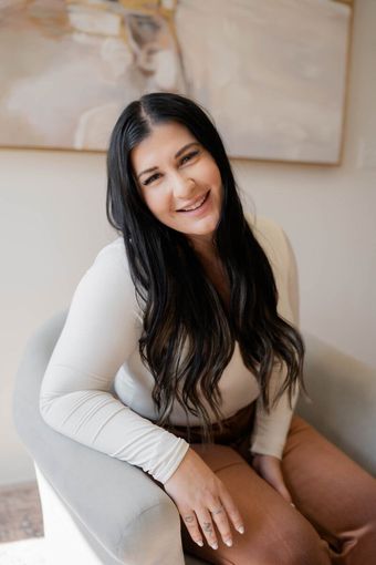 A woman is sitting in a chair in front of a painting and smiling.