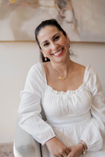 A woman in a white dress is sitting in a chair and smiling.