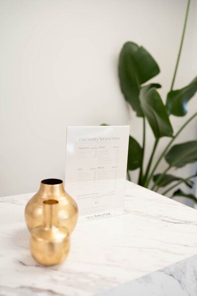 A gold vase is sitting on a table next to a plant.