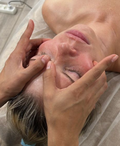 A woman is laying on a bed getting a massage on her face.