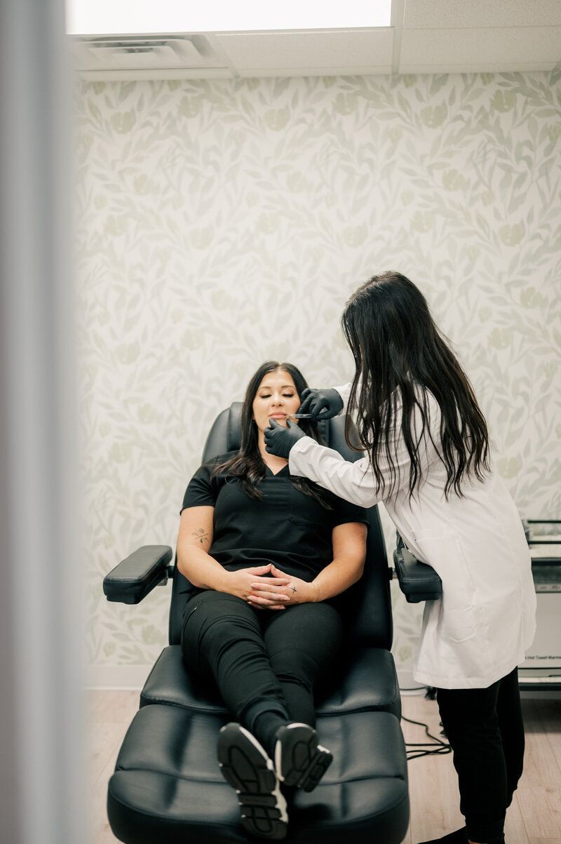 A woman is sitting in a chair while a doctor examines her face.