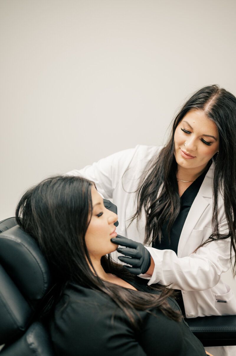 A woman is sitting in a chair while a doctor examines her face.