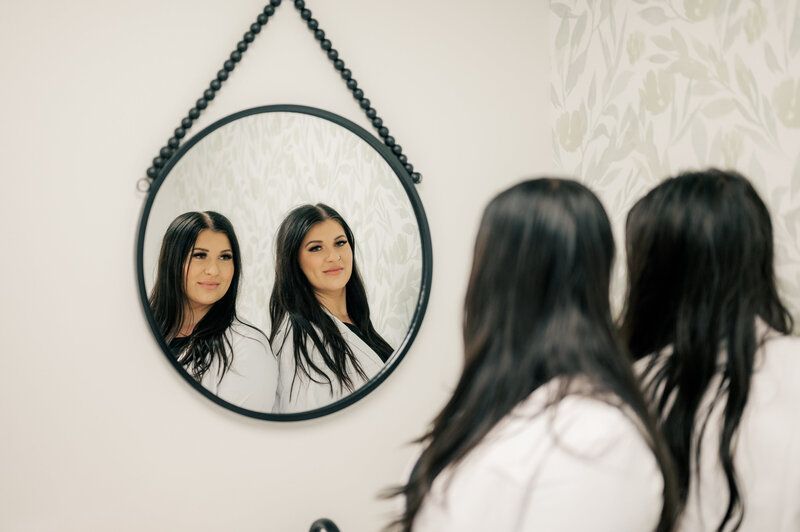 Two women are looking at their reflection in a mirror.