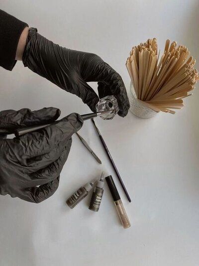 A person wearing black gloves is holding a brush in their hand.