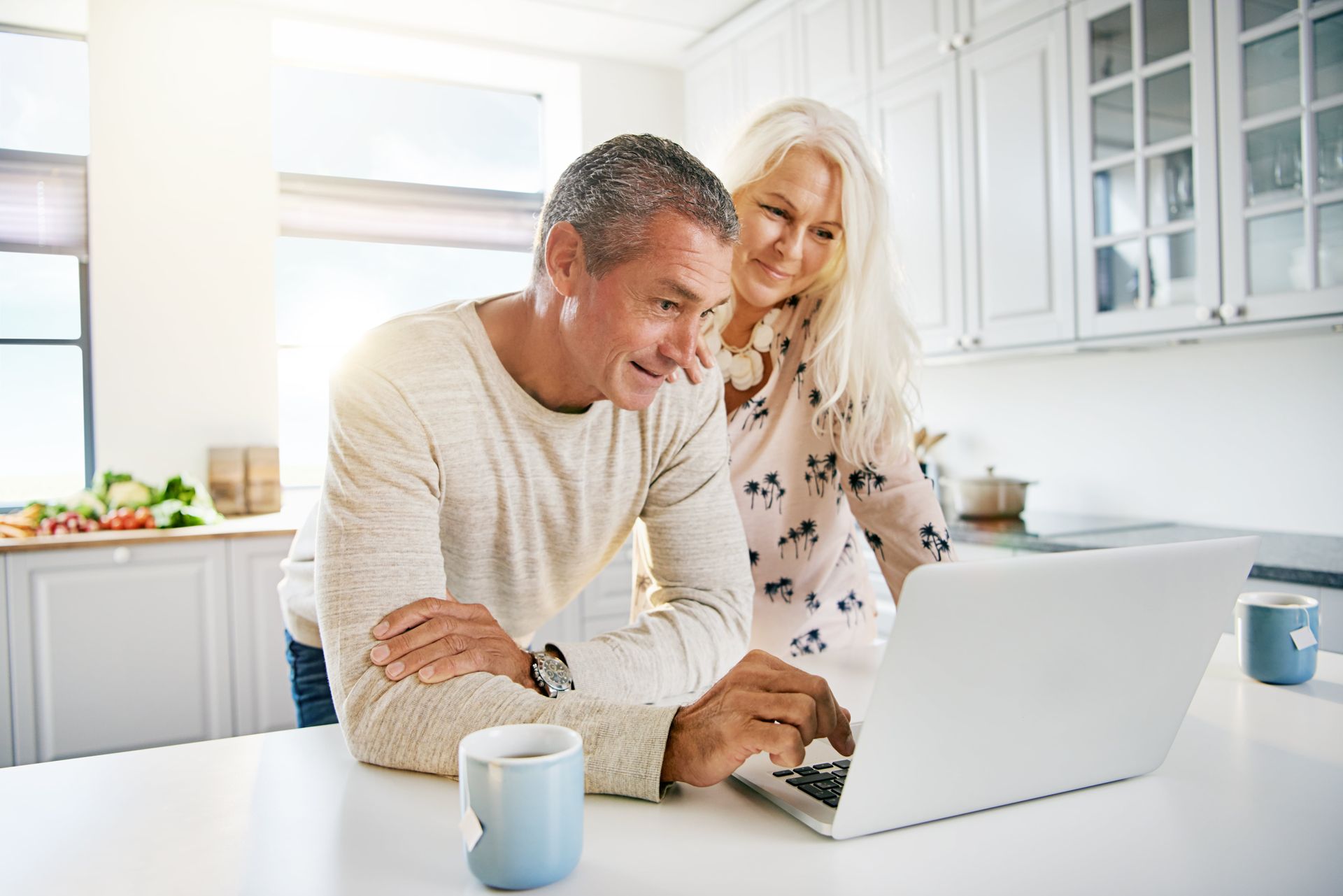 A man and a woman are looking at a laptop computer in a kitchen.