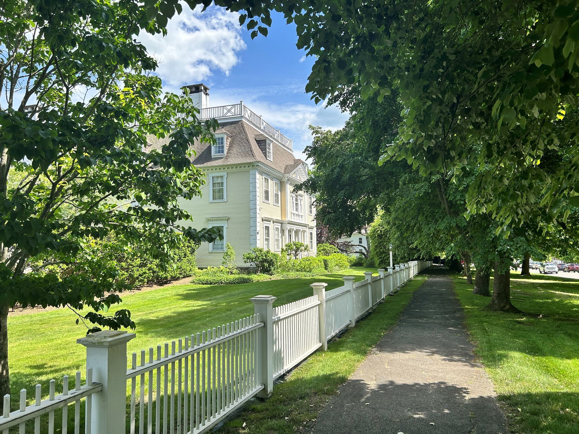 A white picket fence surrounds a path leading to a large house.