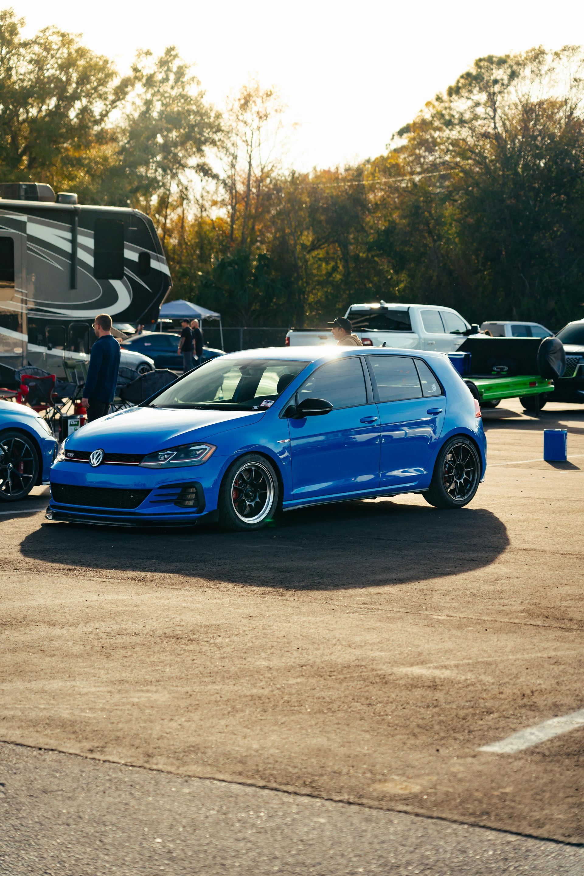 Blue Volkswagen Golf GTI on a paved lot, parked near other cars and trailers.